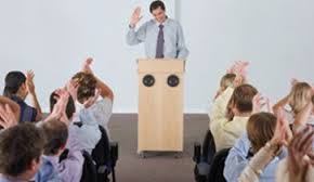 Orateur au pupitre, public qui applaudit